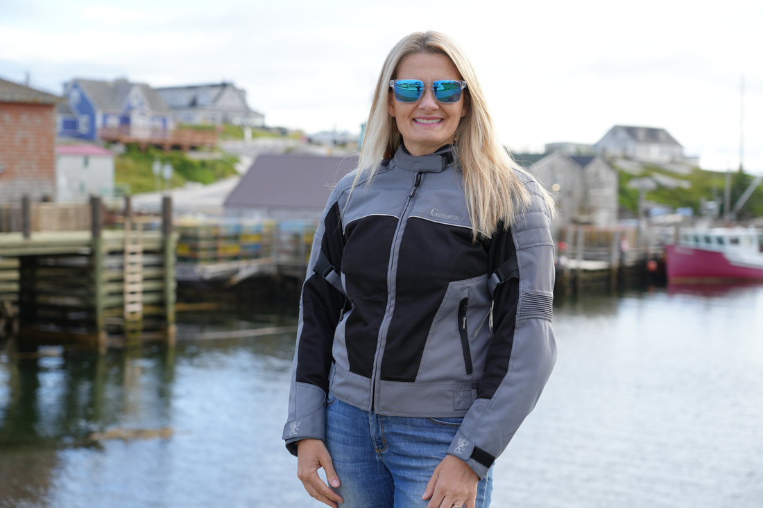 woman standing at a pier wearing a grey gryphon motorcycle jacket and sunglasses 