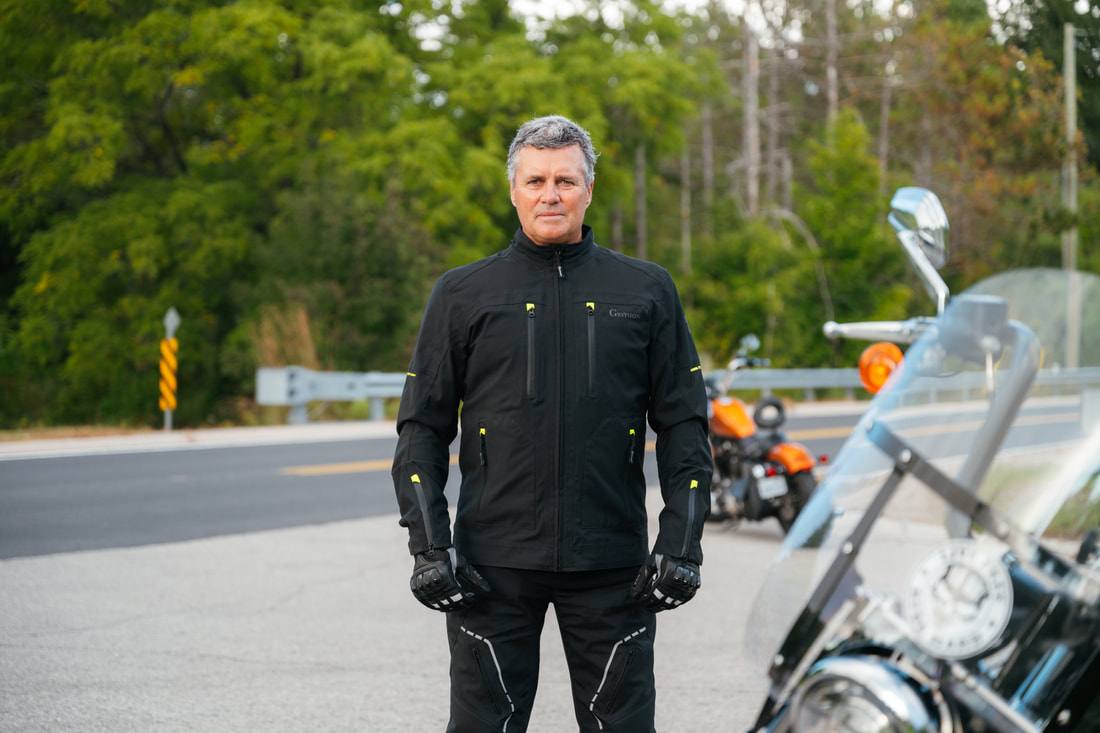 man standing on the road with a motorcycle in front and behind wearing a gryphon motorcycle jacket and gryphon motorcycle pants and gryphon motorcycle gloves