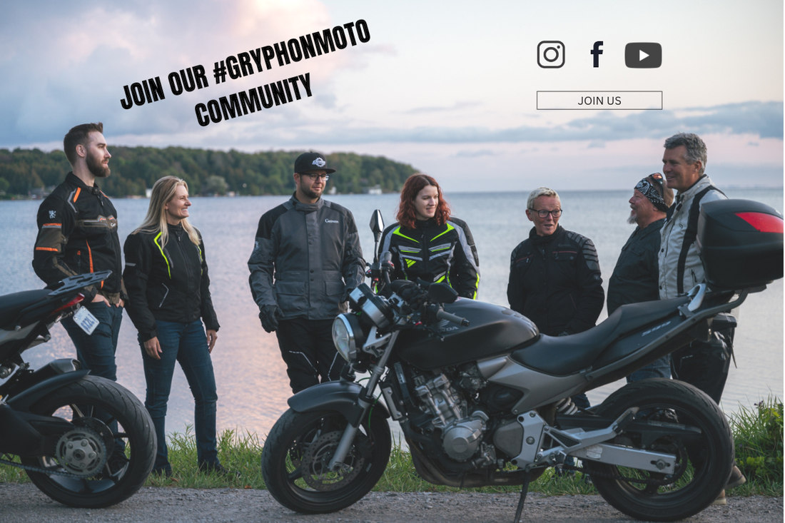 a group of 7 friends gathered behind 2 motorcycles talking to each other and smiling. they are wearing gryphon motorcycle jackets with a lake in the background