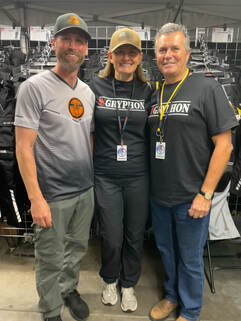 2 men standing on either side of a woman smiling at a motorcycle show wearing gryphon tshirt