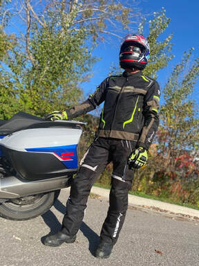 man standing beside his motorcycle on a sunny day with trees in the background wearing gryphon protective motorcycle clothing