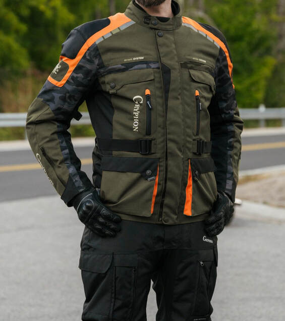 man standing in a driveway with a road and motorcycle in the background wearing a gryphon motorcycle jacket with his hands in his pockets