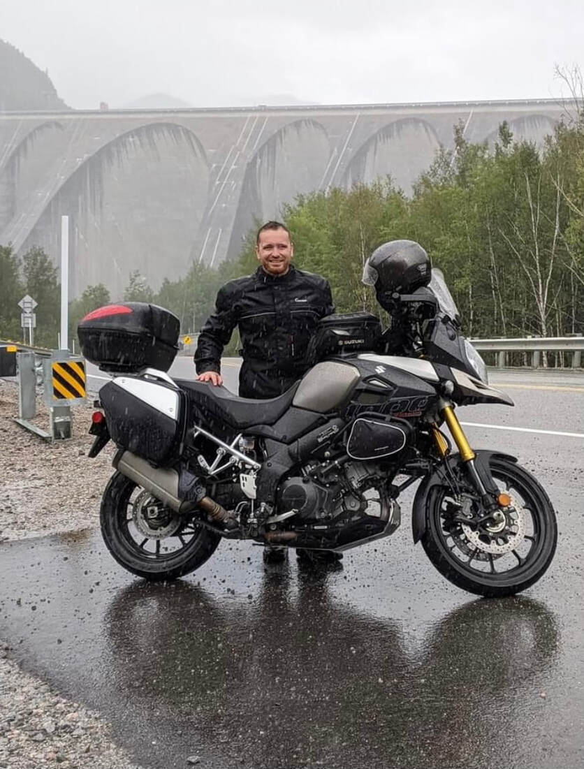 man standing behind his motorcycle in the pouring rain wearing a gryphon motorcycle rain suit 
